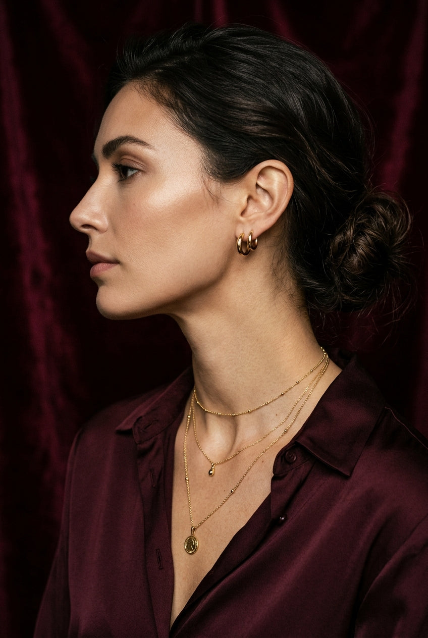 Model wearing layered gold necklaces against burgundy velvet